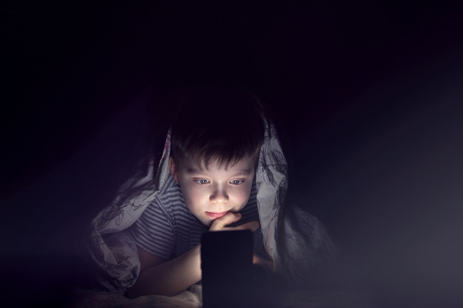 Boy with phone under covers